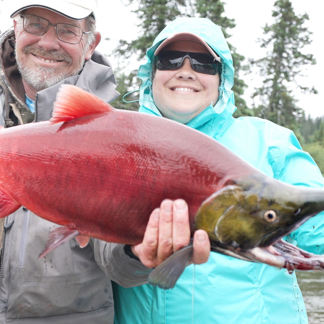 Two smiling guests holding a bright red sockeye salmon