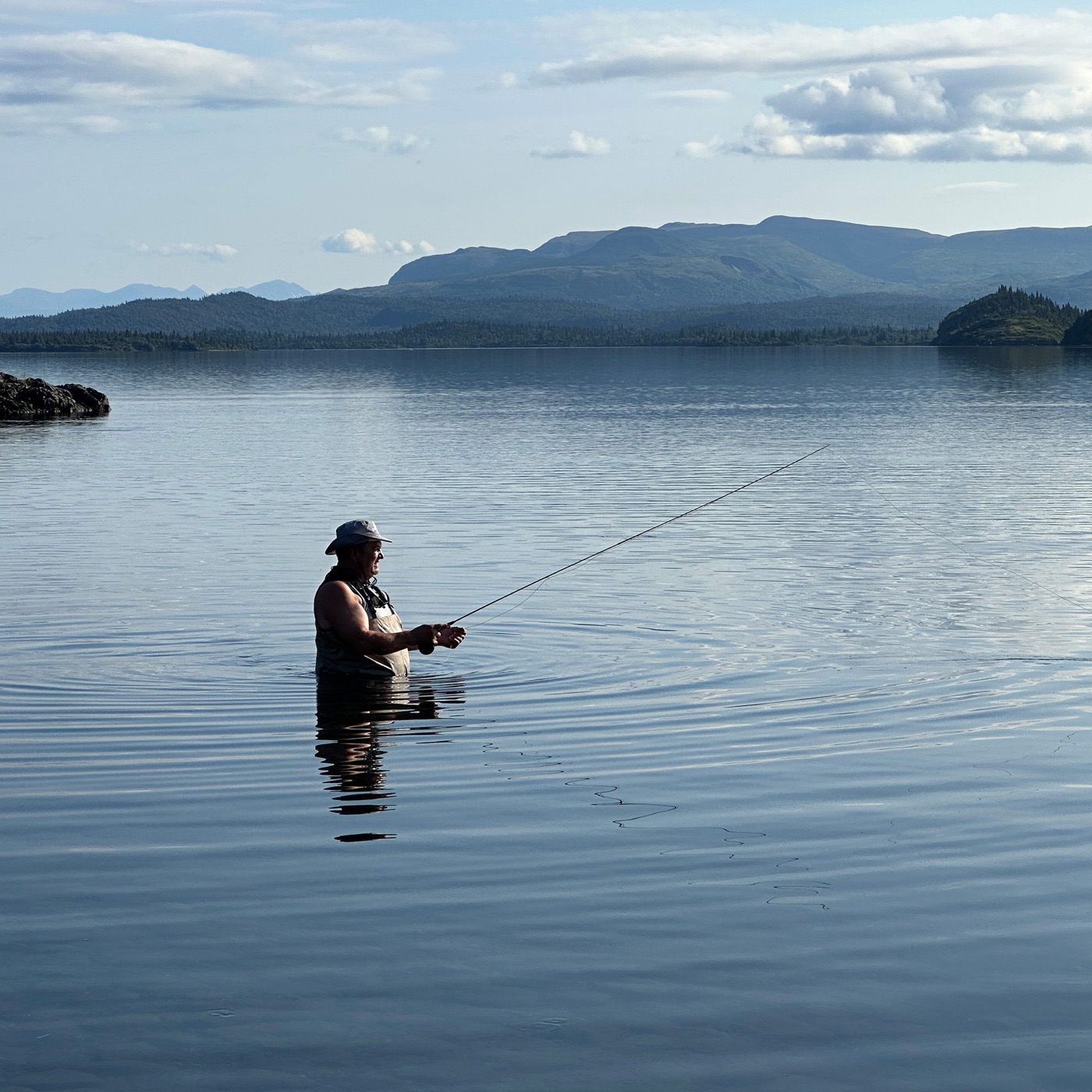 Angler wading in calm Lake Iliamna with mountains behind