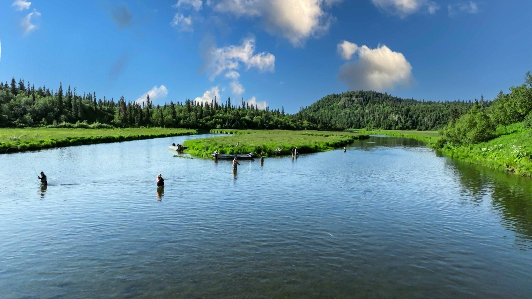 Wide view of anglers wading a river under a blue Alaska sky